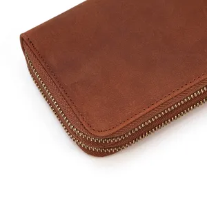Detalle de la cartera de cuero marrón con textura rica y cremalleras metálicas dobles resistentes.