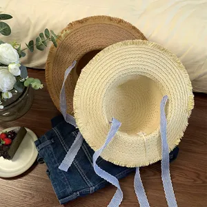 Détail de chapeau de paille plat français avec des rubans à carreaux bleus et bords effilochés.