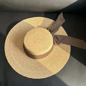 Vue détail du chapeau de paille plat, large bord, nœud ruban marron, plage estivale.