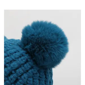 Close-up detail of dark blue knitted winter warm beanie hat with soft fluffy pom pom.