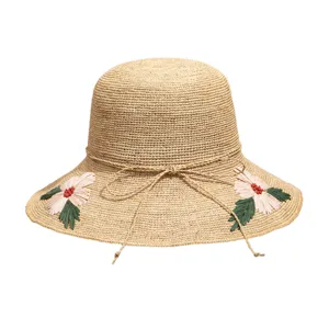 Close-up view of a handmade raffia sun hat featuring delicate floral embroidery and string bow.