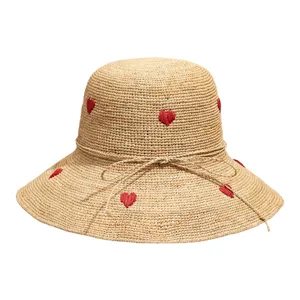 Handmade raffia straw sun hat with cute red heart embroidery and bow detail for summer beach.
