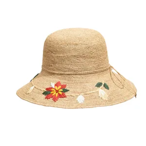Close-up detail of the hand-woven raffia sun hat showing delicate floral embroidery.
