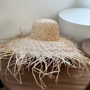 Detailansicht eines Strohhuts mit breiter Krempe und Fransen auf Holztisch für den Sommer.