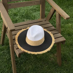 Detailed view of the color-block straw hat with frayed brim on a wooden chair outdoors.