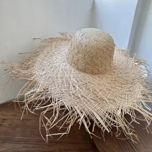 Detailaufnahme eines handgefertigten Strohsonnenhutes mit breiter Fransenkrämpe auf Holztisch.