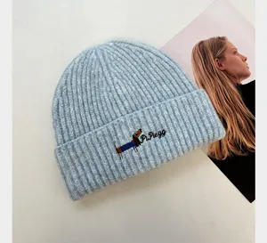 Gros plan sur le bonnet en tricot côtelé bleu clair avec broderie de chiot et détails.