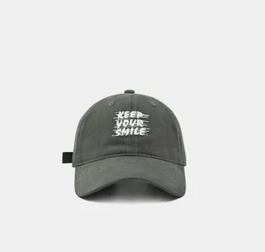 Primer plano de la gorra de béisbol gris oscuro con bordado Keep Your Smile blanco.