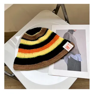 Crochet striped bucket hat detail showing colorful knit pattern and brand label on white chair.