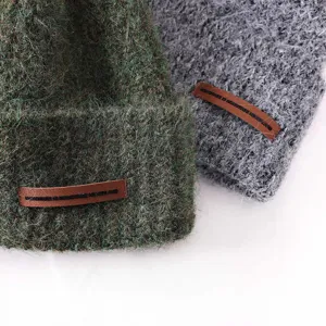 Detailed view of thick warm fuzzy knit beanie hat in green and grey with leather brand patch.