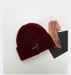 Gros plan détaillé du bonnet en tricot marron bordeaux avec broderie de chiot et côtes.