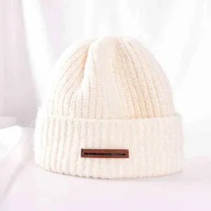 Close-up detail of warm beige knitted winter beanie hat with brown leather label accent.