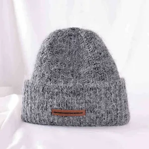 Detailed view of grey fuzzy knitted beanie hat with brown leather tag, cozy winter headwear.