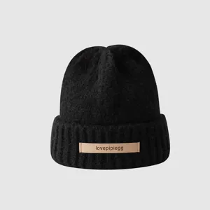 Close-up detail view of the black knitted winter beanie featuring a stylish leather label.
