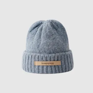 Close-up of blue knitted beanie hat detail showing soft wool texture and front leather label decoration.