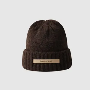 Close-up detail of the brown knitted beanie with a front leather label and soft texture.