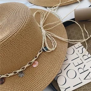 Detailed shot of a straw boater hat with braided ribbon and shell pendants for summer beach vacation.