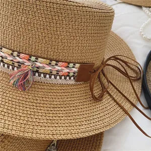 Close-up detail of a stylish straw boater hat featuring colorful woven band, tassels, and leather strap.