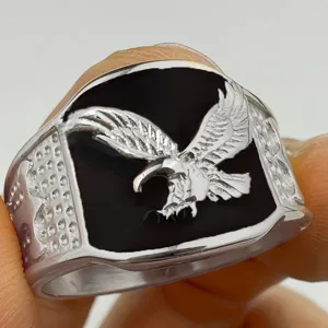 Primer plano del anillo de águila de plata para hombre con esmalte negro y banda lateral texturizada.