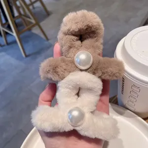 Gros plan de pinces a cheveux en peluche moelleuse avec grande perle pour un style hivernal chic.