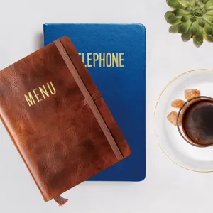 Gold 3D metal letter stickers detail view on leather notebooks with coffee and plant scene.