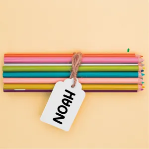 Detalle de lápices de colores con etiqueta de papel personalizada sobre fondo beige claro