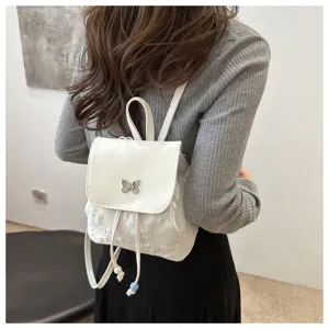 Vue détaillée d'un sac à dos blanc compact avec pendentif papillon et fermeture à cordon.