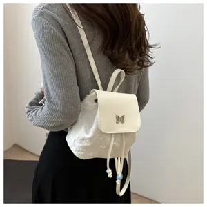 Vue détaillée du mini sac à dos de mode blanc avec un joli charme de papillon en métal et cordon.