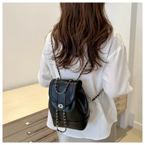Détail de sac à dos en cuir noir avec bretelles en chaîne tressée et fermoir métallique.