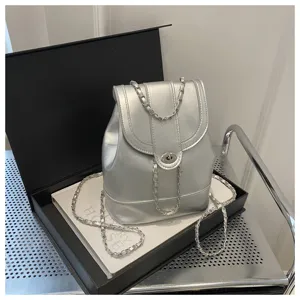 Détail de mini sac à dos argenté métallisé avec bretelles chaîne et fermoir tournant.