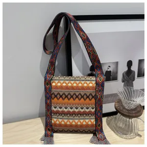 Sac à bandoulière tissé ethnique rétro avec sangle large et détails de glands, style vintage.