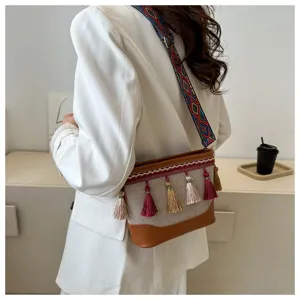 Détail de sac porté épaule en toile bohème, sangle tissée ethnique et pampilles colorées.