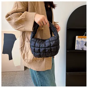Détail de sac à main matelassé noir, texture douce et poignée courte style tendance.