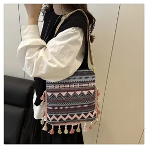 Détail de sac bandoulière tissé ethnique, avec motifs géométriques et pompons ludiques.