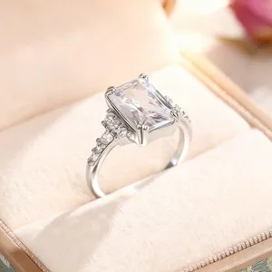 Elegante anillo de circonita con talla esmeralda y piedras brillantes en terciopelo.
