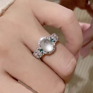 Close-up of vintage style oval moonstone ring with sparkling pavé diamonds and green stones.