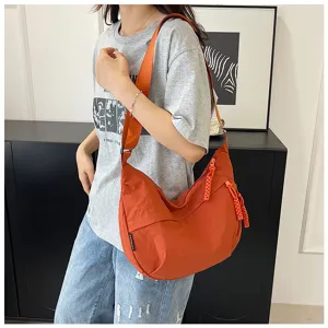 Gros plan d'un sac dumpling tendance en nylon orange porté par le modèle en intérieur.