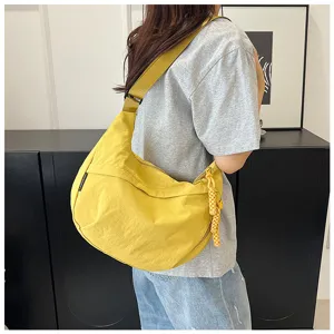 Vue détaillée du sac bandoulière en nylon jaune avec sangle large et charm tressé.