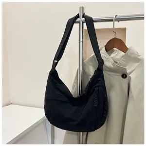 Vue détaillée du sac à épaule en nylon noir suspendu au portant, design décontracté.