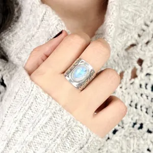 Close-up detail of vintage wide silver carved ring with glowing oval gemstone on finger.