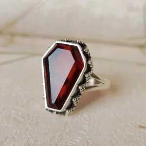 Primer plano del anillo gótico punk en forma de ataúd con gema roja y detalles plateados.
