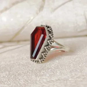 Anillo de estilo punk vintage con forma de ataud y piedra roja con detalles plateados.
