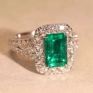 Primo piano dell'anello vintage con smeraldo e diamanti halo su sfondo neutro e testurizzato.