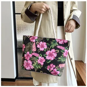 Detail view of black canvas tote bag with pink tropical floral print and white rope handles.