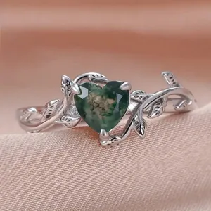 Primer plano de anillo corazón de ágata musgosa verde con diseño de rama delicada.