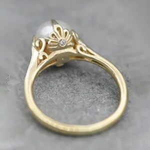 Vista detallada del anillo de perla dorada vintage con intrincado patrón de filigrana y diamante.