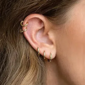 Primer plano detallado de pendientes de aro dorados apilados y brazaletes de oreja.