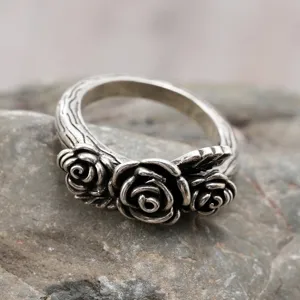 Detail shot of vintage silver rose ring featuring three flower motifs and wood texture.