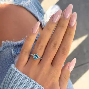 Primo piano dell'anello in zircone blu in stile oceano indossato al dito con unghie rosa.