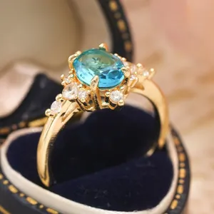 Primo piano dettagliato di un delicato anello dorato con gemma blu ovale e zirconi brillanti.